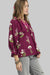 Woman wearing a plum-colored blouse with floral patterns on a white background